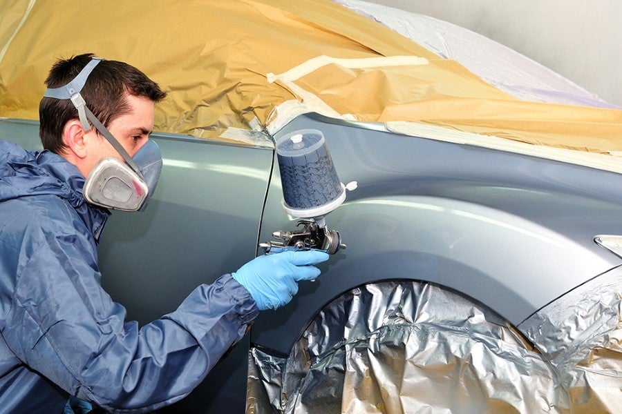 A man in a blue suit is painting a car with a spray can in a well-lit garage.